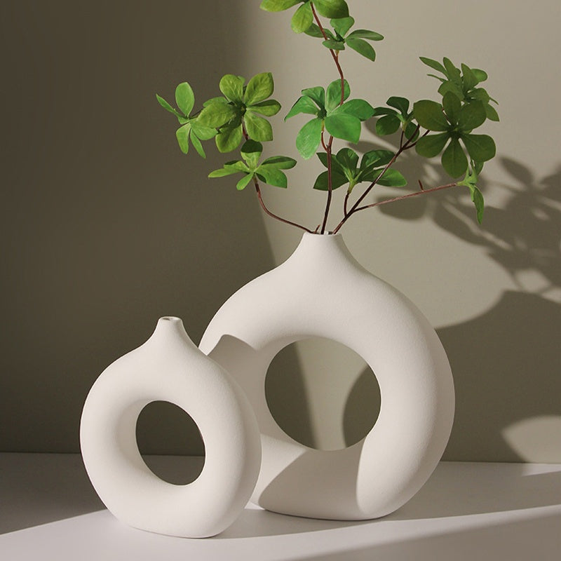 Pair of white donut vases in two sizes with green stems, soft shadow on the wall