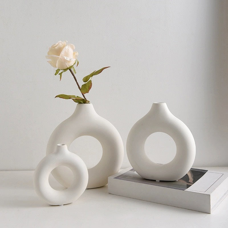 Three white donut vases of different sizes with a single rose, on a book